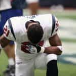 An NFL player in uniform takes a knee.