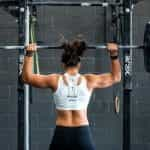 A female bodybuilder lifts weights from behind.