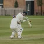 Man in white clothing hits a cricket ball with a bat.