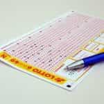 A lottery playing card lying flat on a table with a pen placed on top of it.