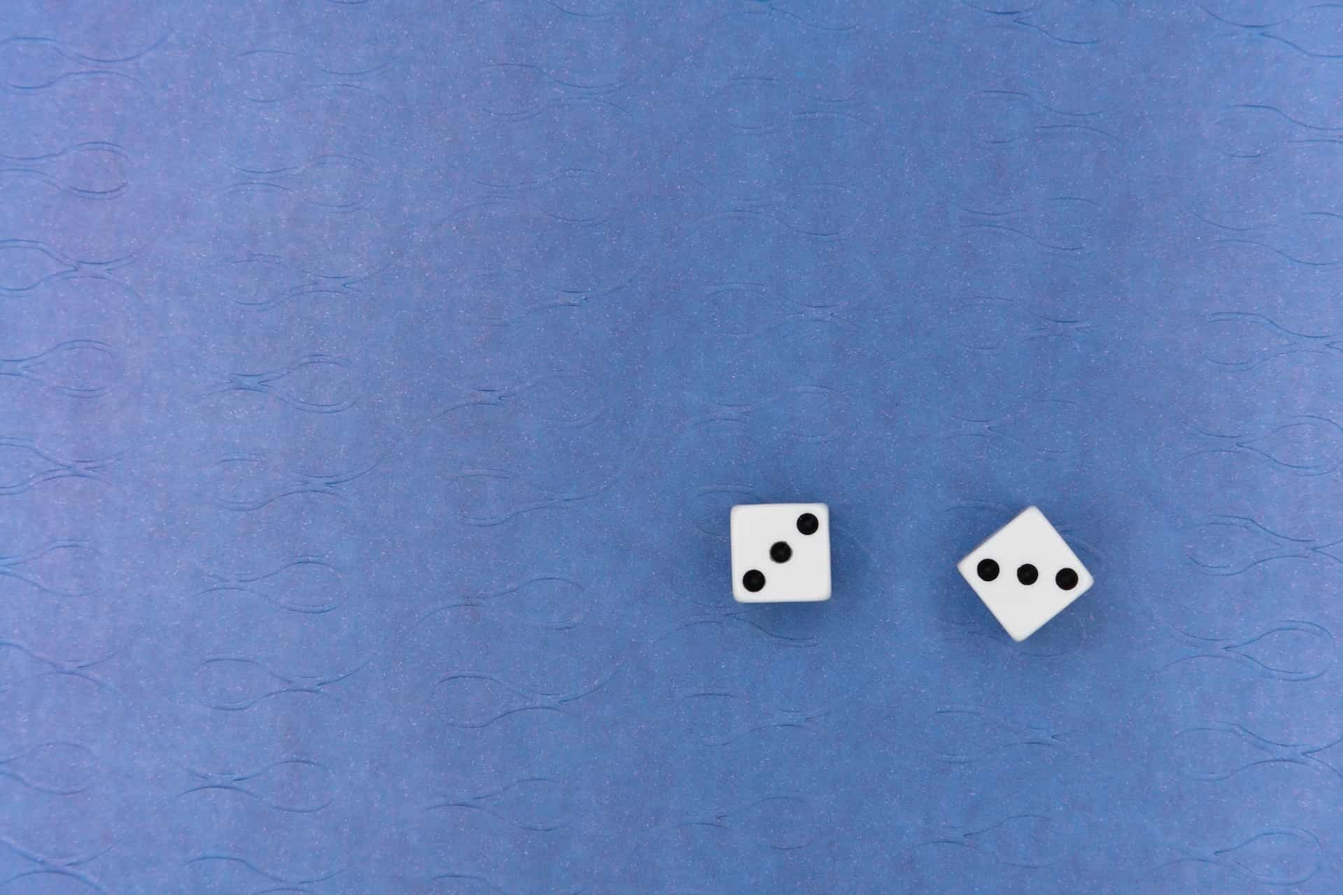 Two white dice small on a blue surface.