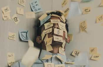 A man leaning against a wall, both of which are covered in dozens of post-it notes with various life affirmations and motivational slogans.