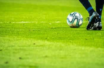 A ball and a pair of soccer player’s legs and shoes on grass.