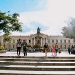 People walk in front of a government building with columns in El Salvador.